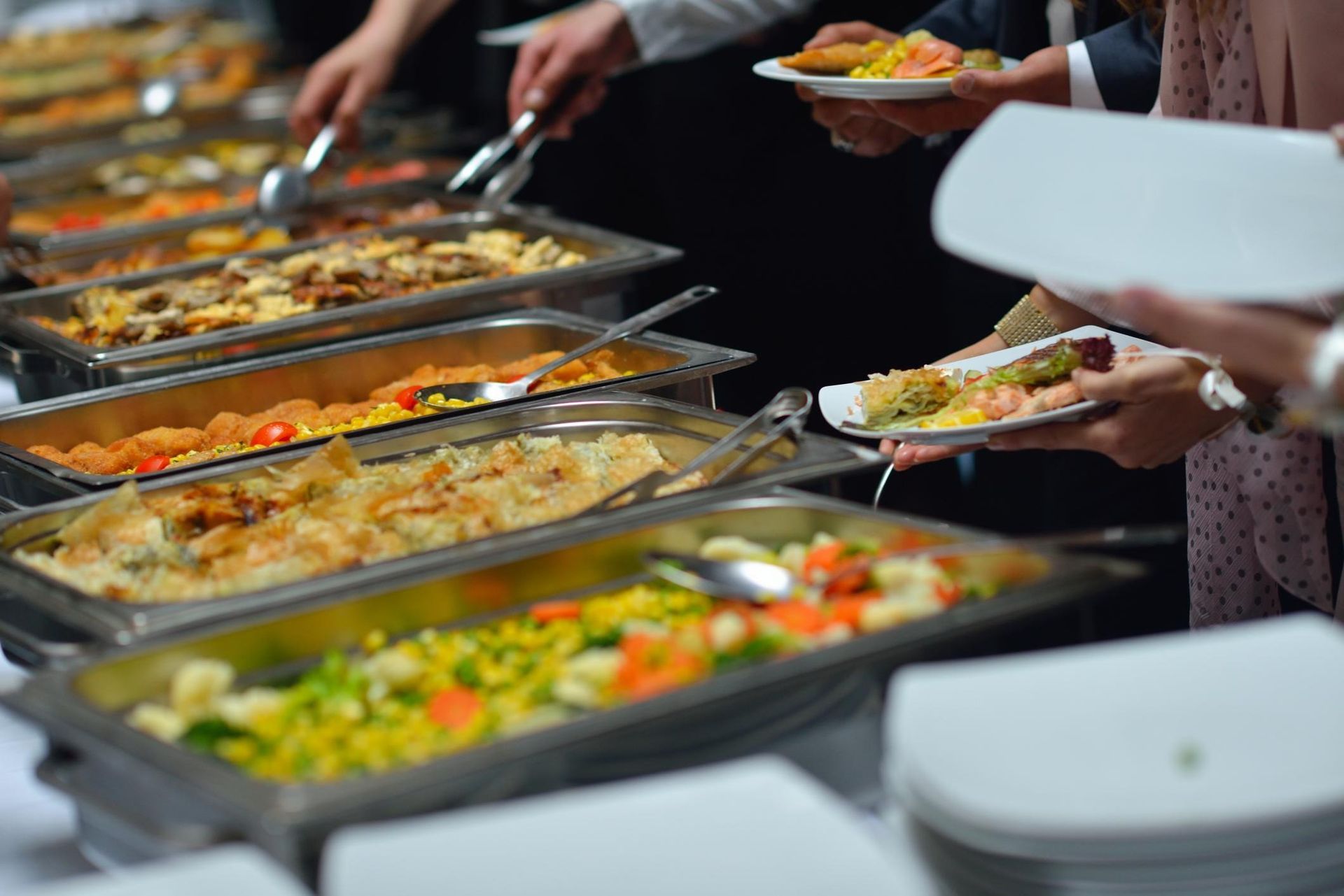 People serving food from buffet trays onto white plates at a catered event