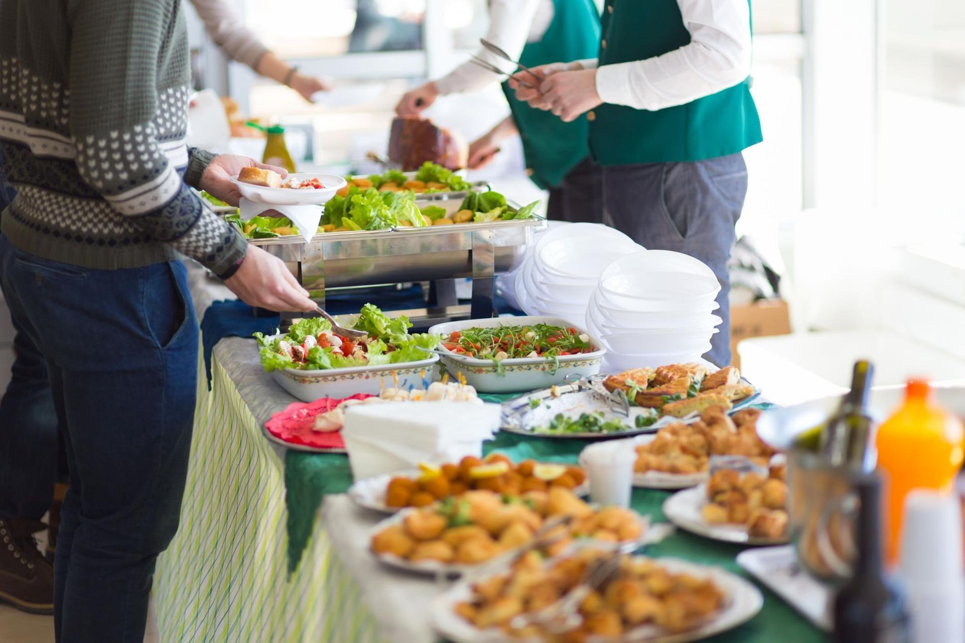 People serving buffet-style salads and appetizers on a long table at an indoor event