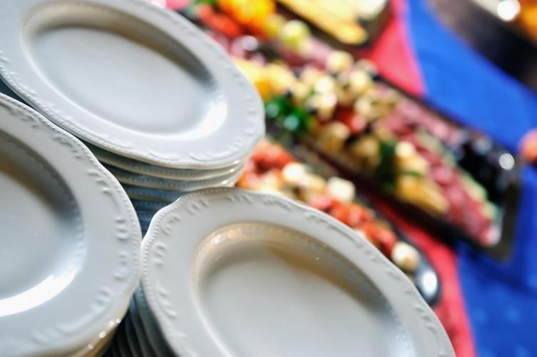 White disposable plates with colorful food platters on a blue tablecloth