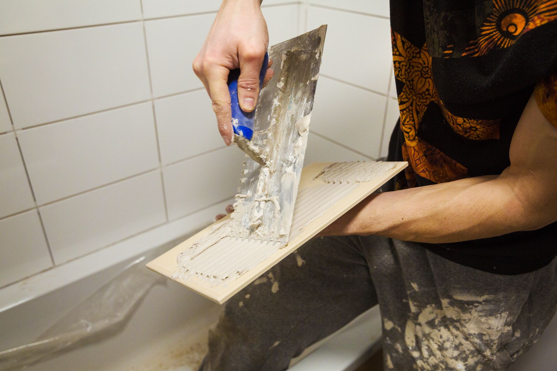 Fliesenleger Badezimmer Fliesenleger trägt mit der Zahnkelle präzise Fliesenkleber auf eine keramische Fliese auf