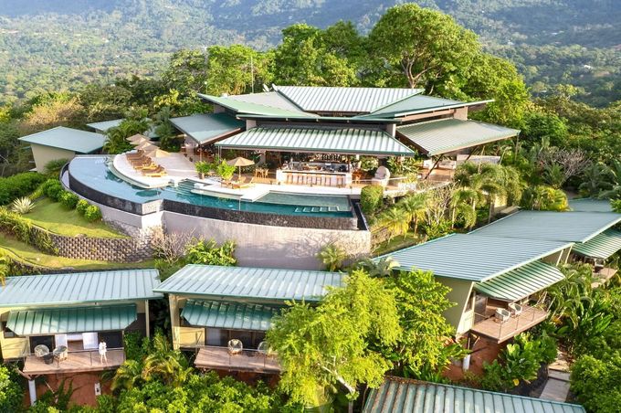 Luxury resort with green rooftops nestled in lush, mountainous terrain, with an infinity pool.