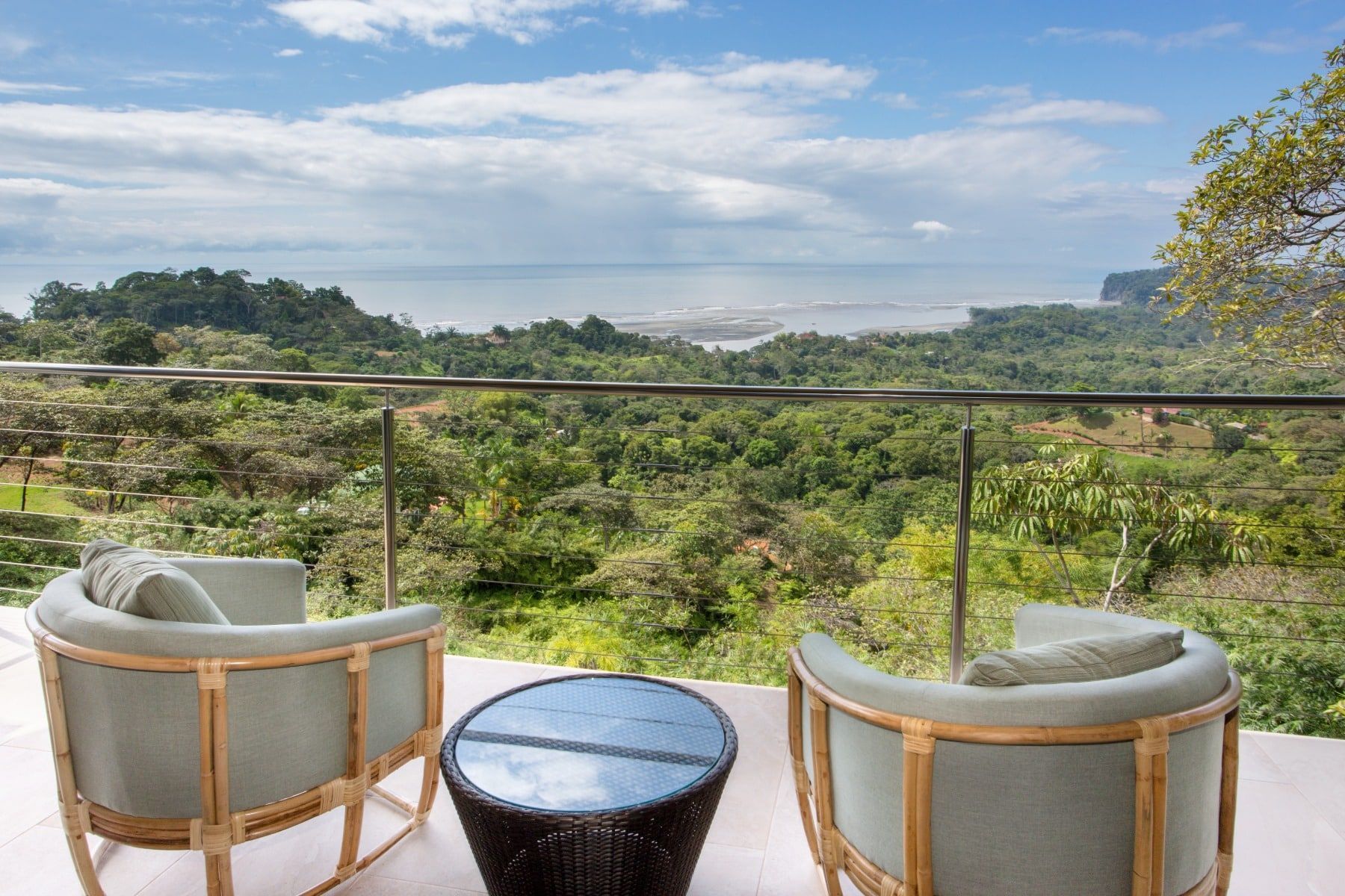 Two chairs and a table on a balcony overlooking a lush green forest.