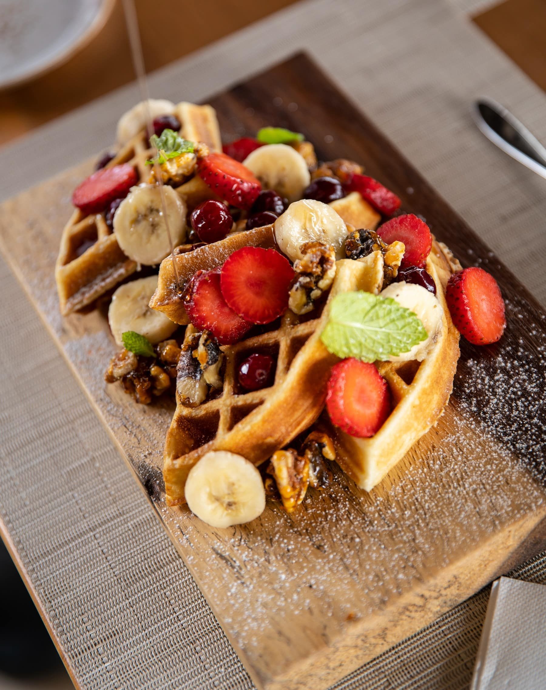 A wooden cutting board topped with waffles and fruit