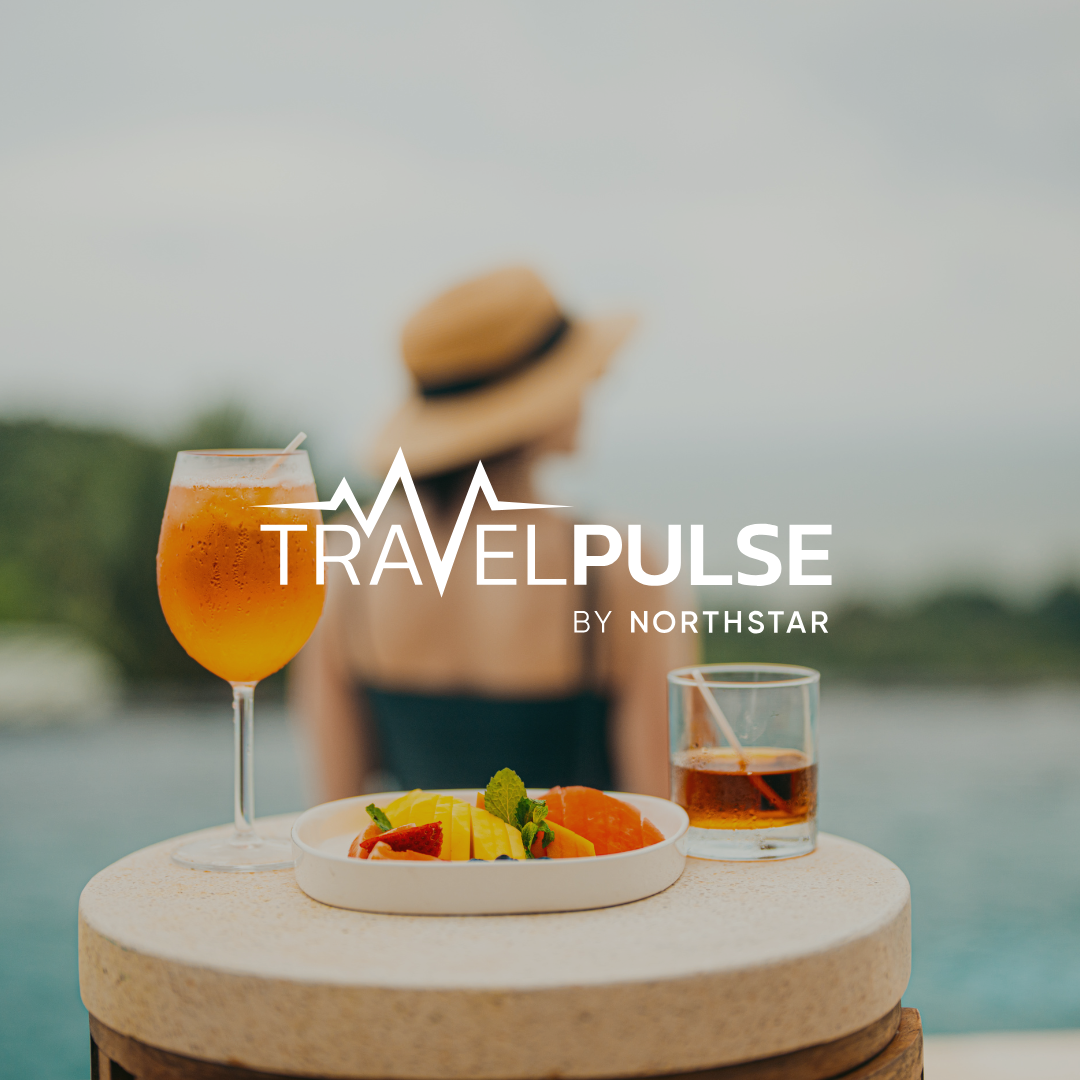 A woman with a hat by a pool enjoys a cocktail and fruit.