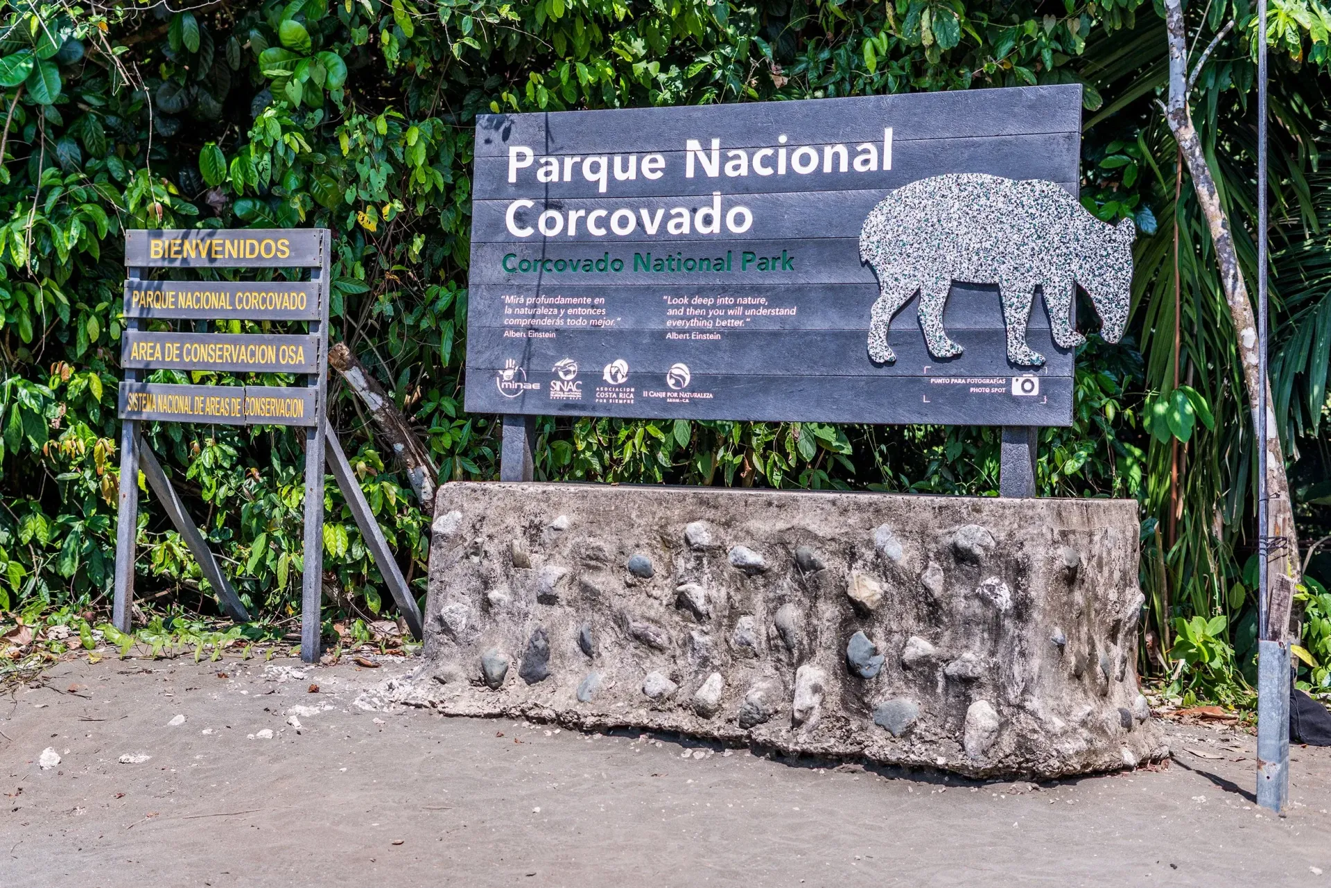Entrance sign for Parque Nacional Corcovado beside a stone base and forest trail