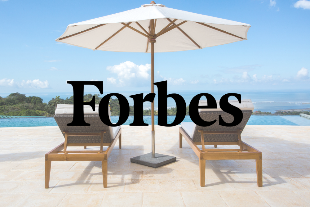 A white umbrella is sitting on top of a patio next to a swimming pool.