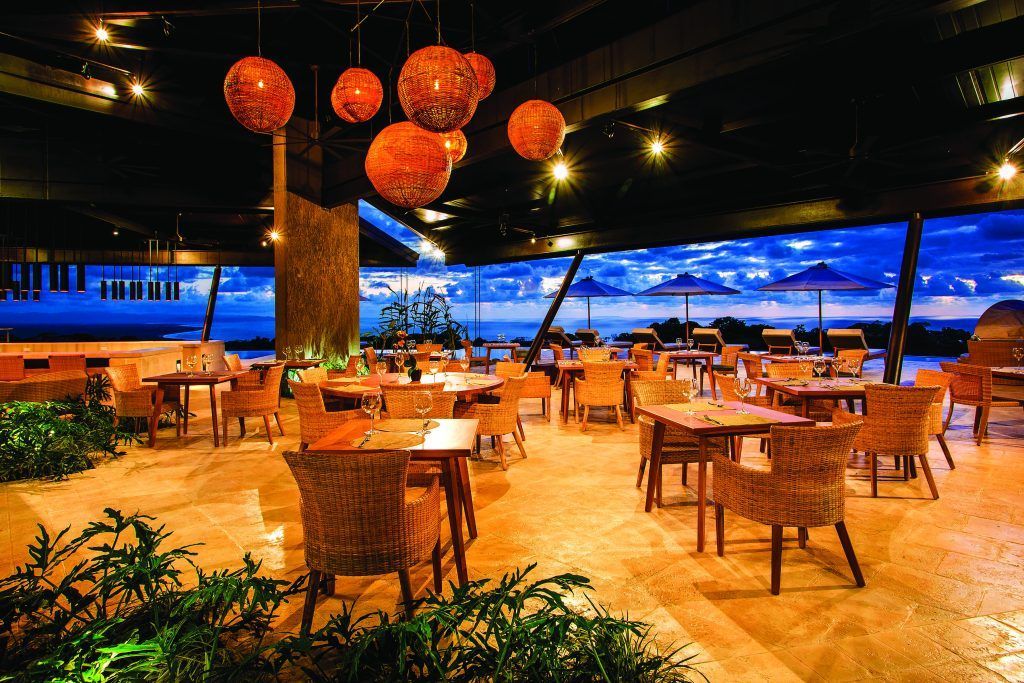A restaurant with tables and chairs and a large window with a view of the ocean.