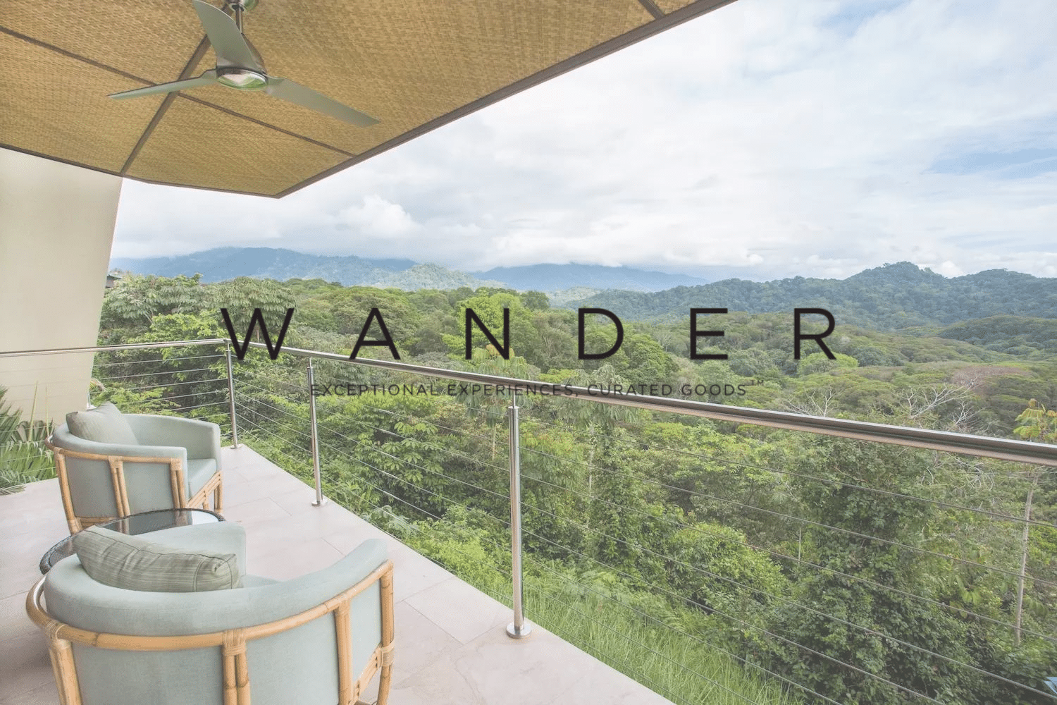 A balcony with chairs and a ceiling fan overlooking a lush green forest.