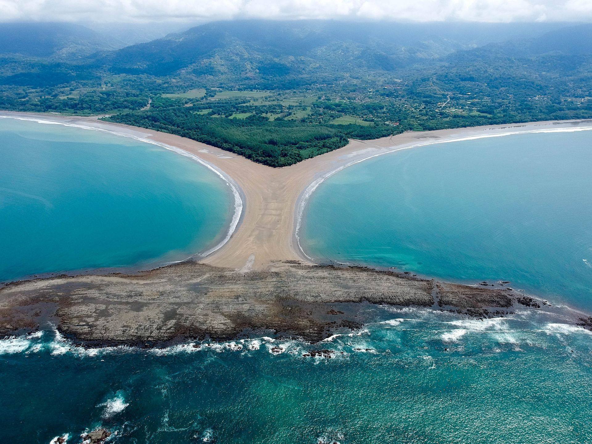 An aerial view of the famous Whale Tail sandbar in Uvita, Costa Rica, surrounded by turquoise water and lush forest.