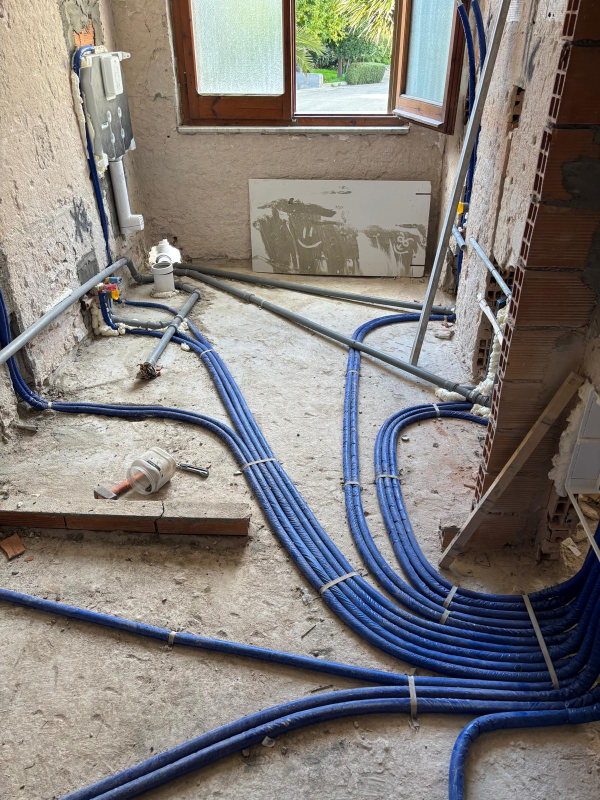 Una stanza in fase di ristrutturazione con numerosi tubi di plastica blu posati sul pavimento, che conducono a un apparecchio a parete.