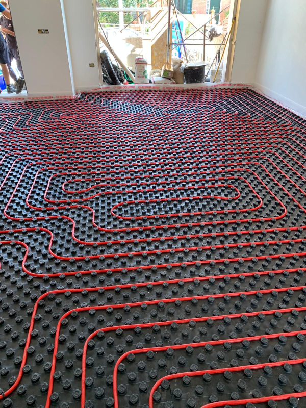 Tubi arancioni per il riscaldamento a pavimento installati a griglia su una base di plastica scura all'interno di una stanza in fase di ristrutturazione.