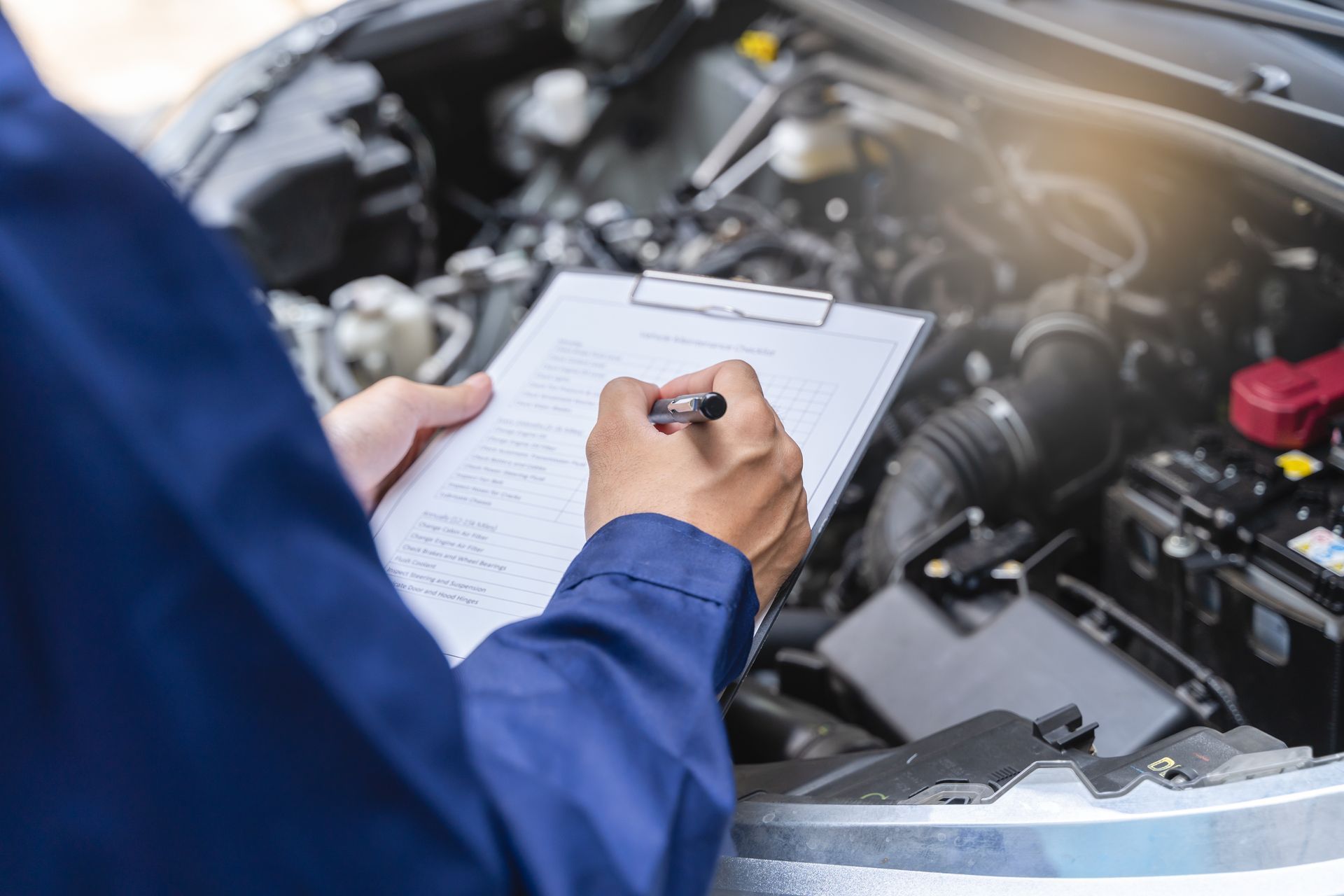 Vehicle Inspection — O'Fallon, MO — O'Fallon Garage Technician writing notes on a clipboard by an open hood for transmission repair