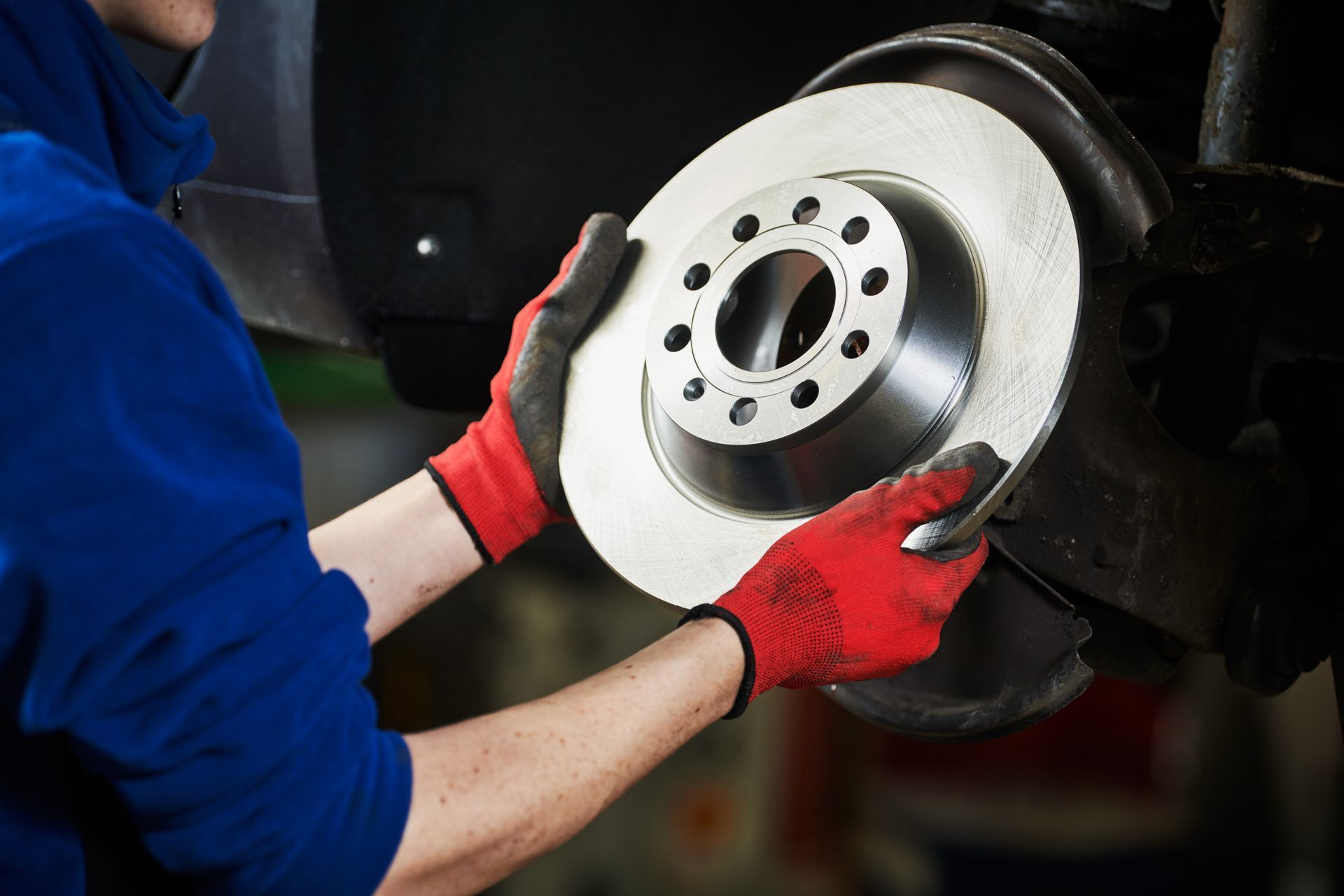 A mechanic performing brake repair services, holding an automobile brake disk for replacement.