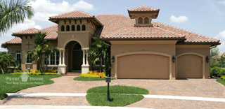 A tan Mediterranean-style house with a paver driveway, terracotta roof, and a palm tree in the front yard.