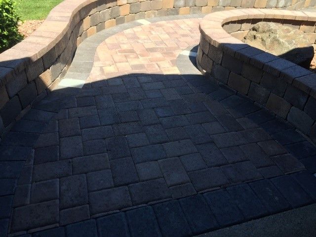 A stone patio with a curved retaining wall and a patterned walkway leading toward a landscaped area with rocks.