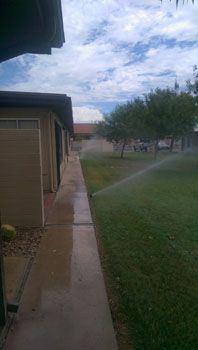 A sprinkler is spraying water on a lush green lawn in front of a house.