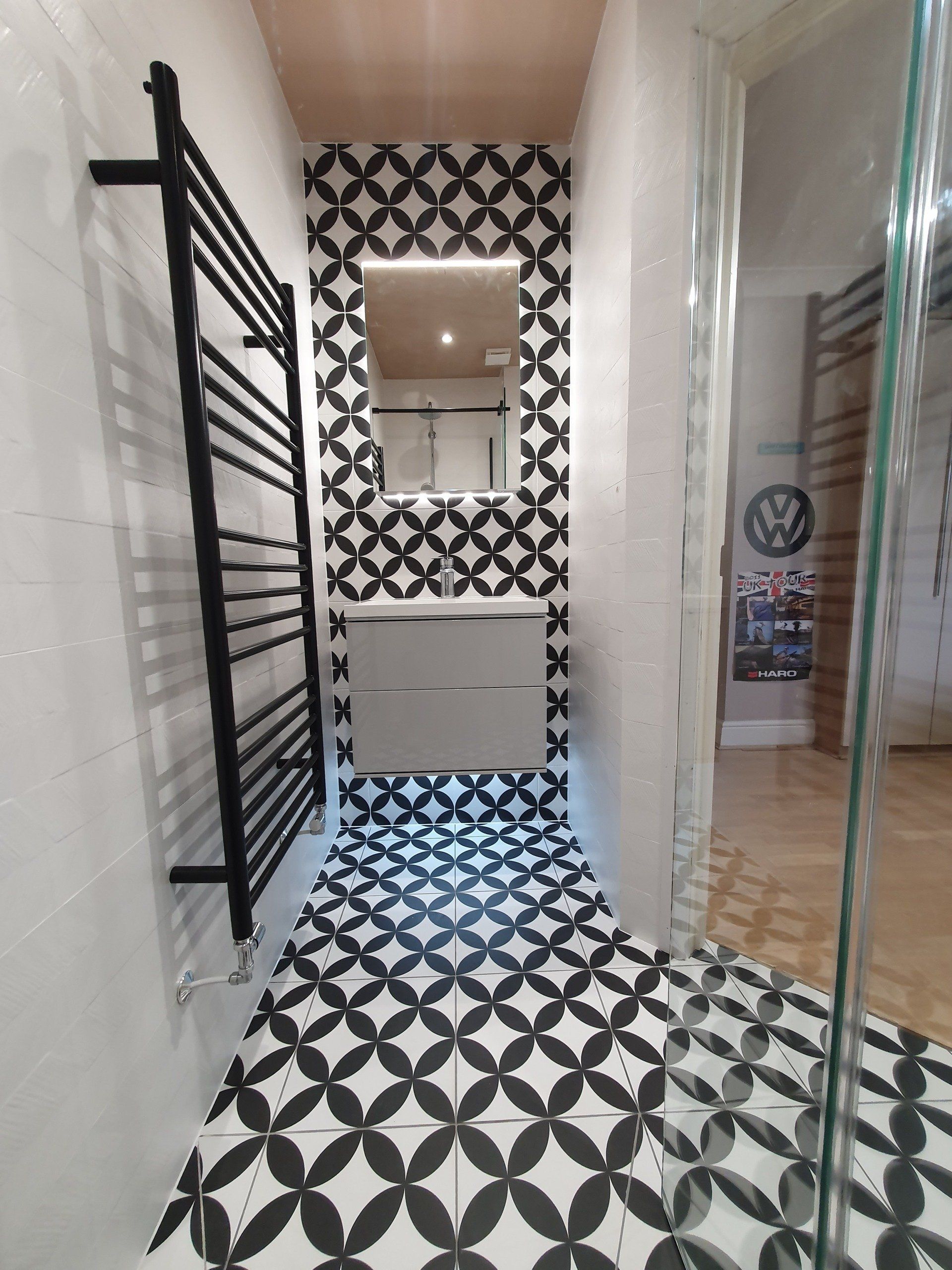 Long modern bathroom with walk-in shower and black-and-white patterned flooring.