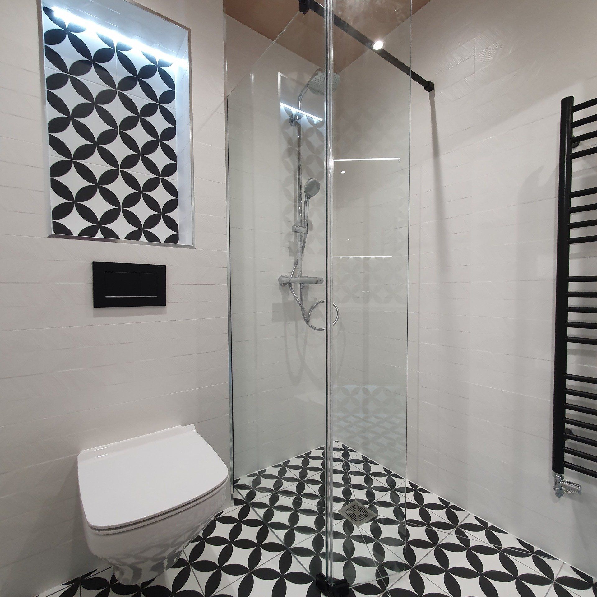 Compact monochrome bathroom with walk-in shower, wall-hung toilet and patterned tiles.