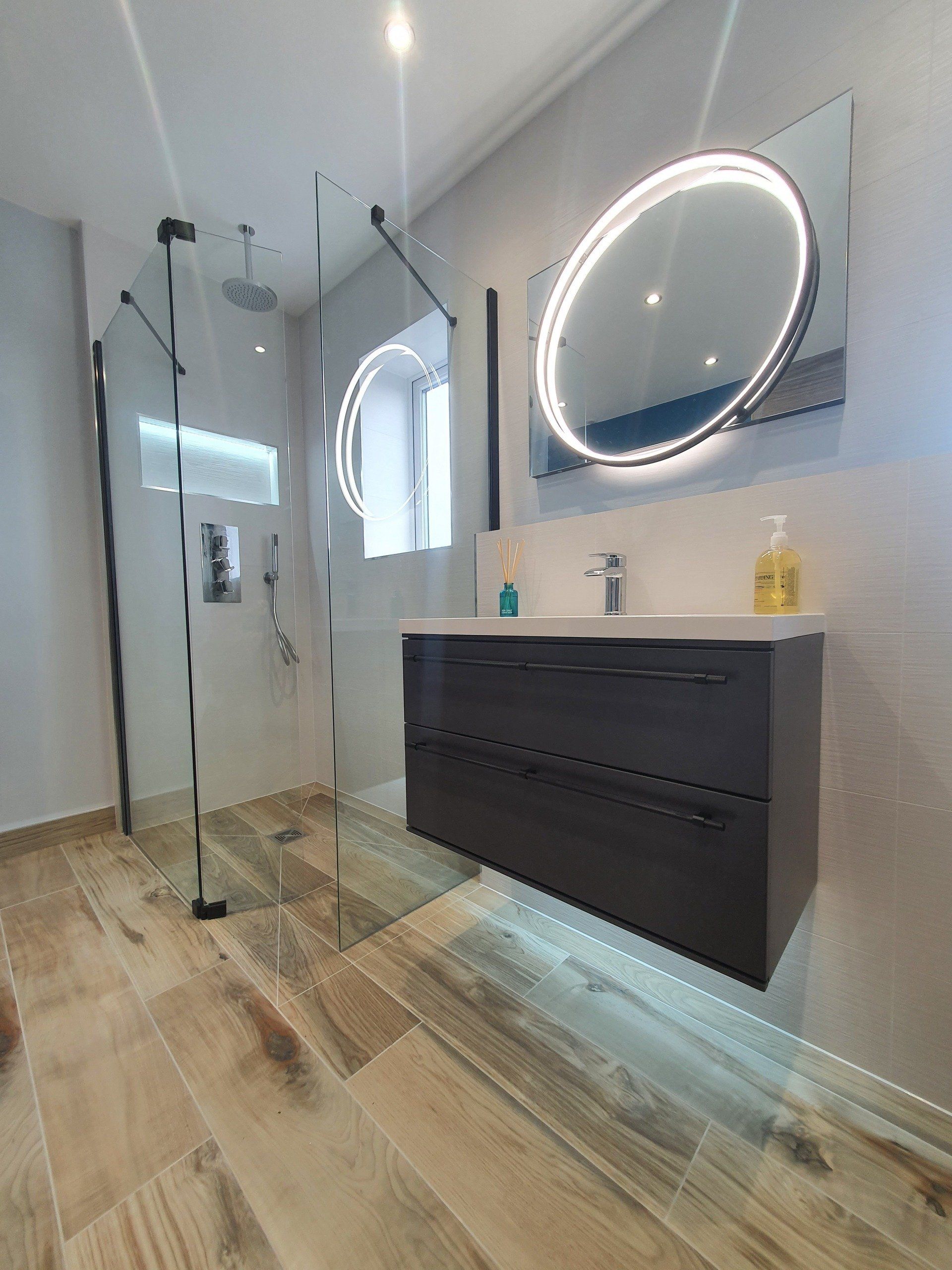 Modern bathroom with floating vanity, illuminated mirror and walk-in shower.