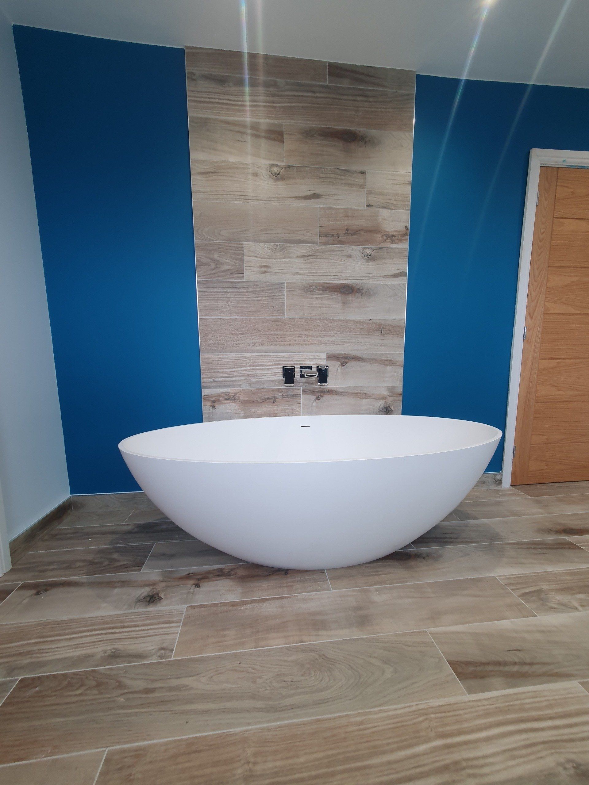 Freestanding bath against a blue feature wall with wood-effect flooring.