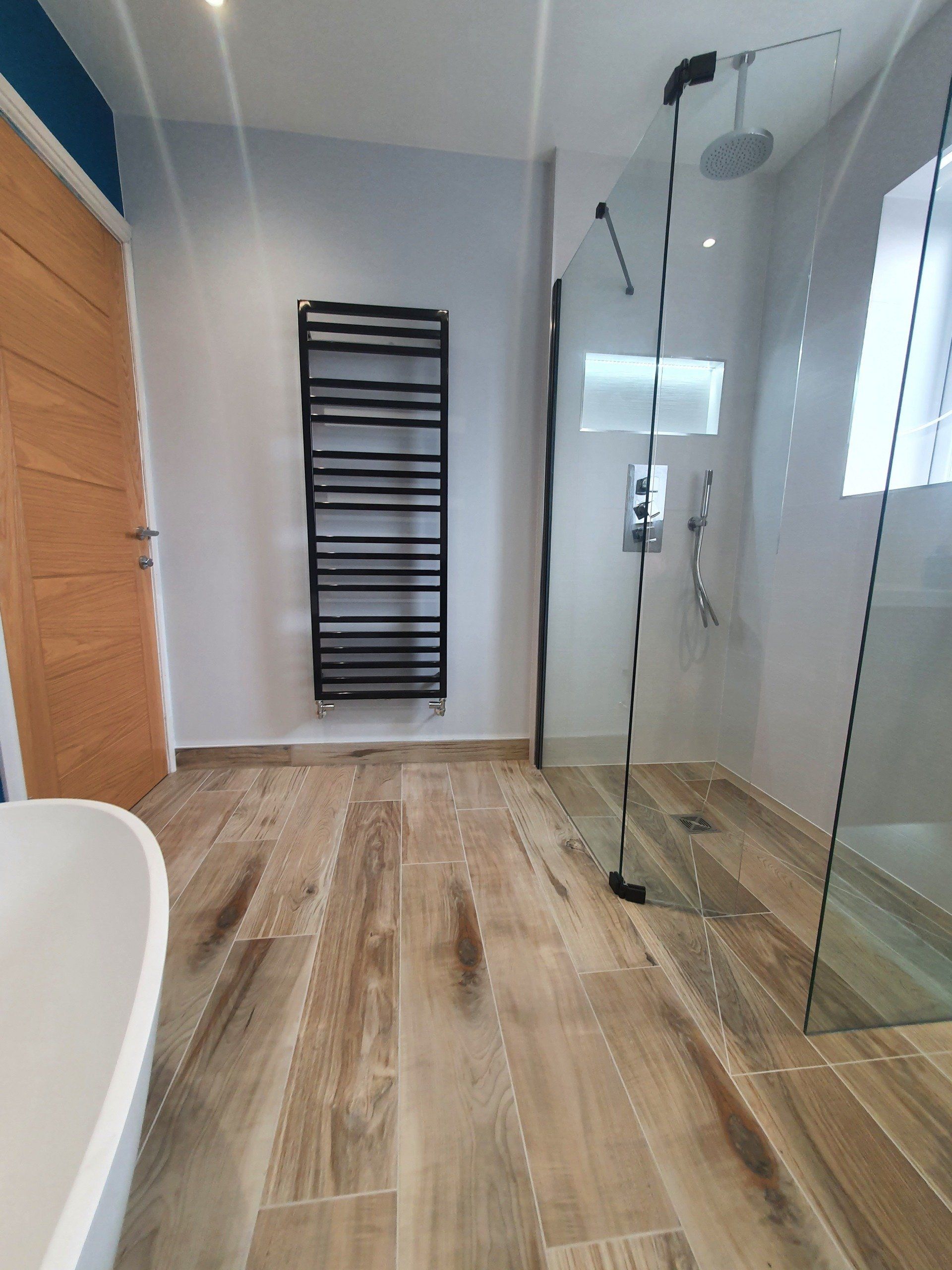 Contemporary bathroom with glass shower, black towel radiator and wood-effect floor.