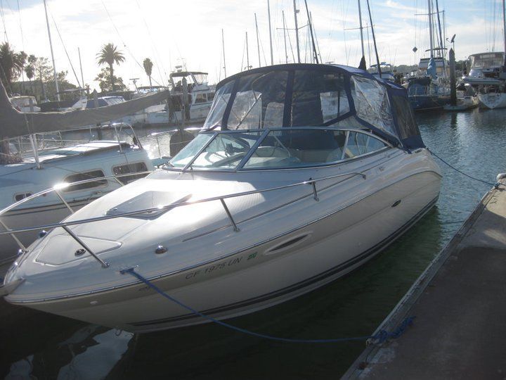 A white boat with a blue canopy is docked in a marina