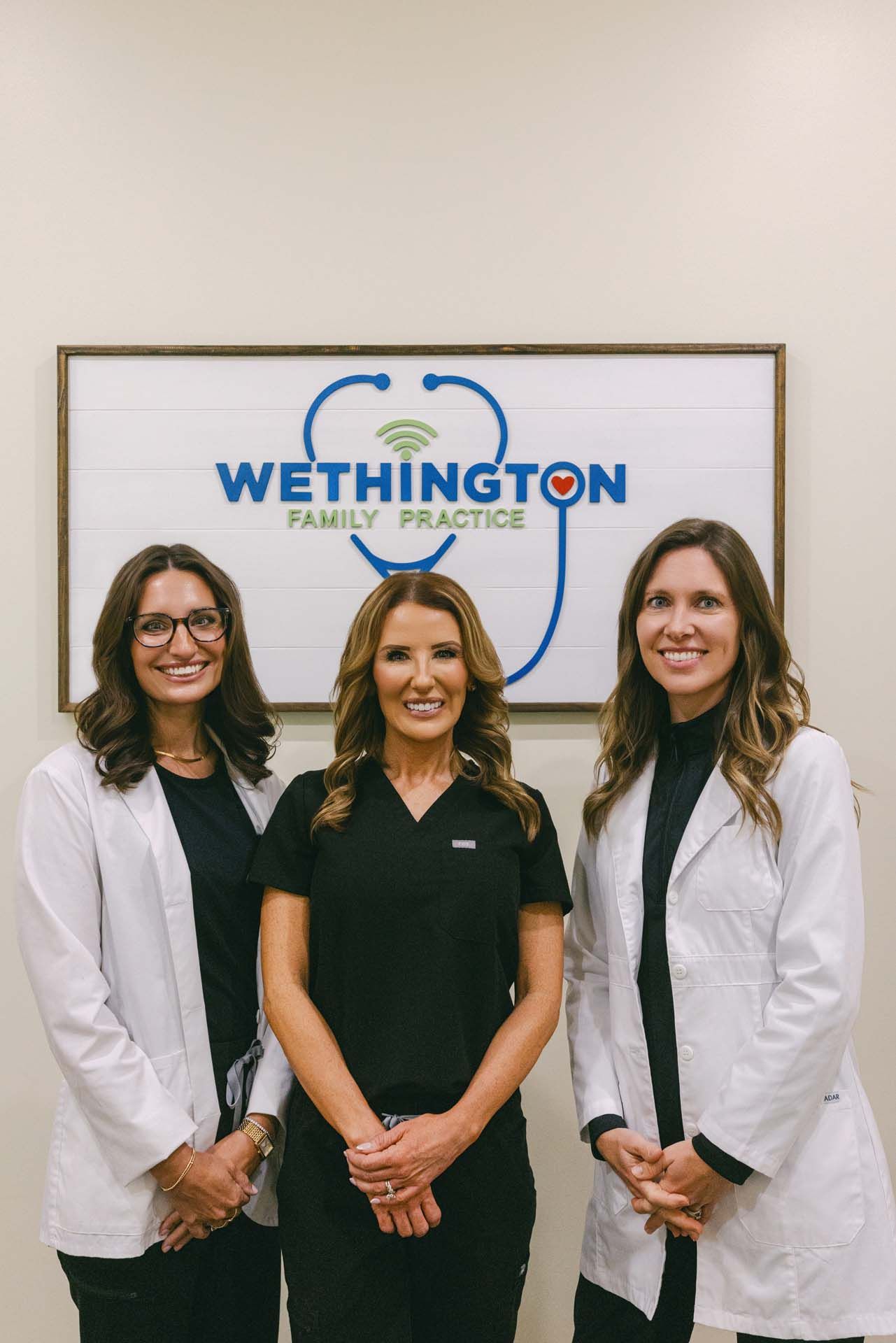 Three clinicians standing in white coats in front of a Wethington Family Practice sign