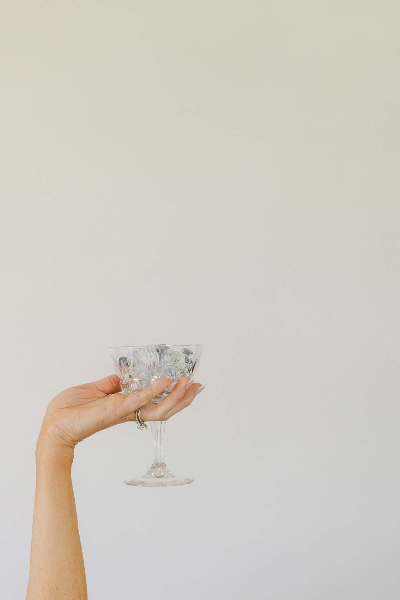 Hand holding a clear, patterned stemmed glass against a plain light wall