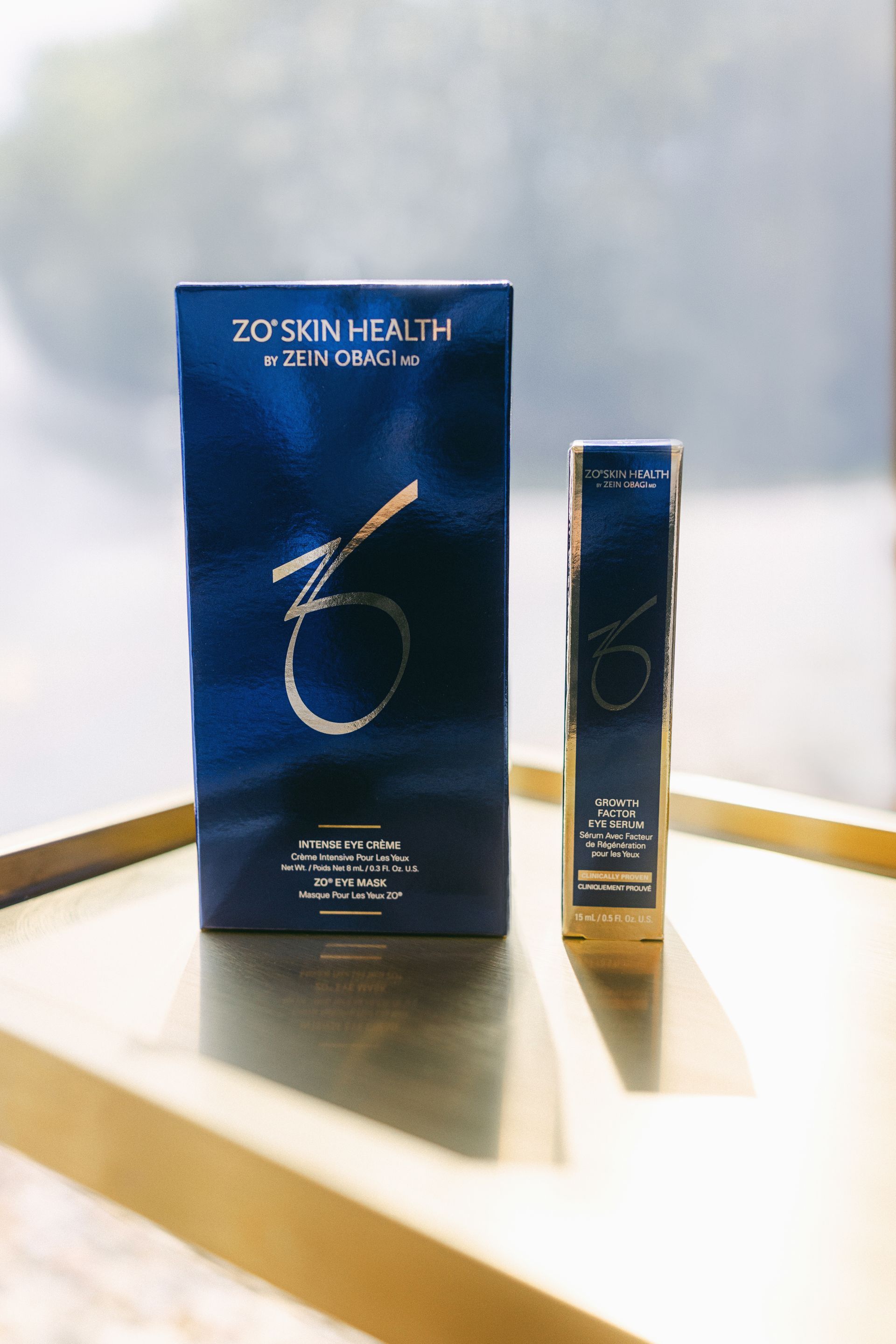 Blue cosmetic product box and tube standing on a bright surface with gold diagonal shadows.
