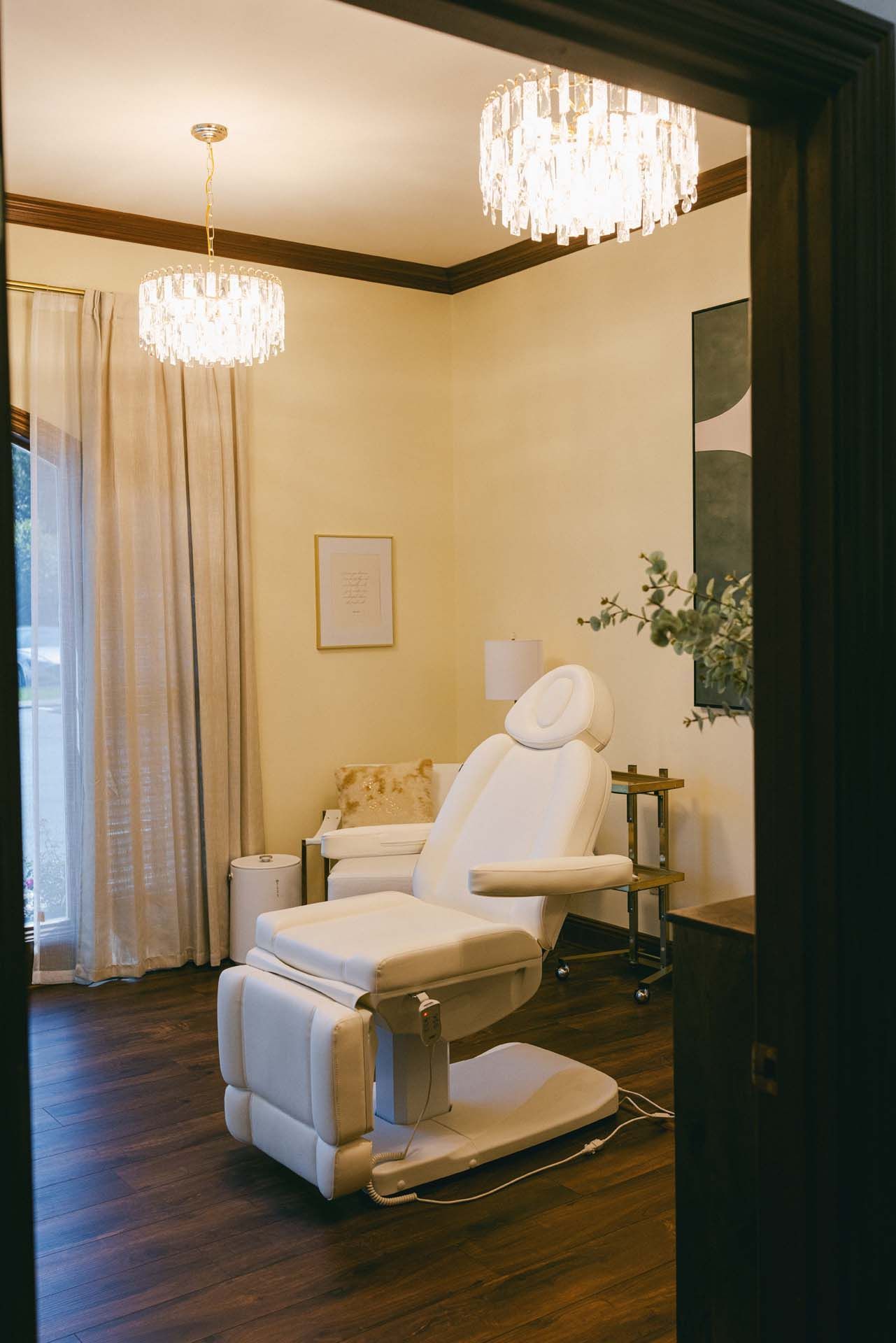 Modern treatment room with a white reclining chair, chandeliers, and soft beige walls