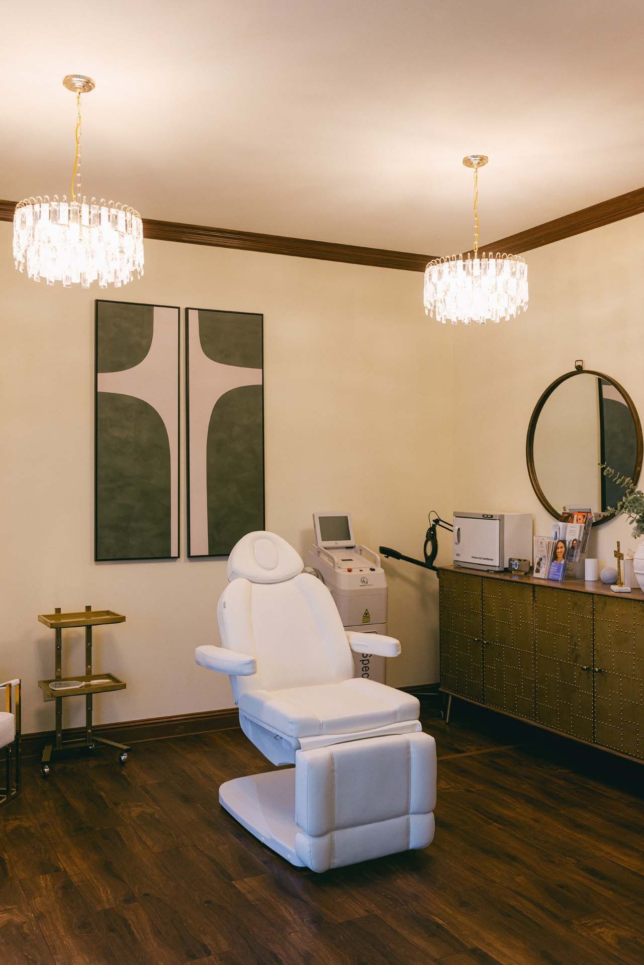 Modern spa treatment room with a white reclining chair, chandeliers, and a vanity table with mirror