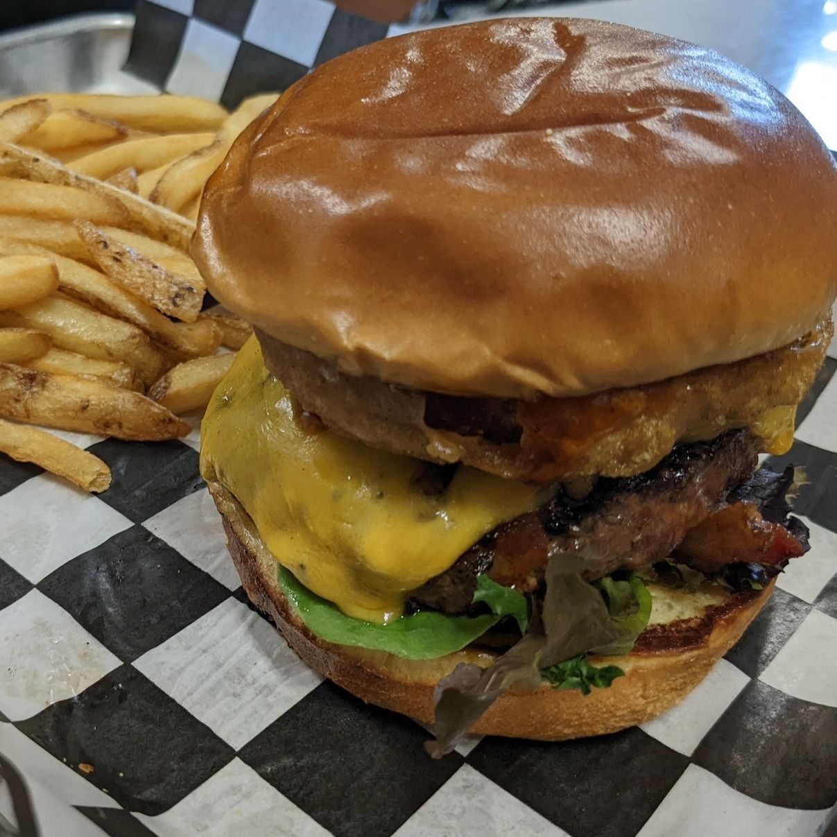 Cheeseburger with onion ring and fries on checkered paper.