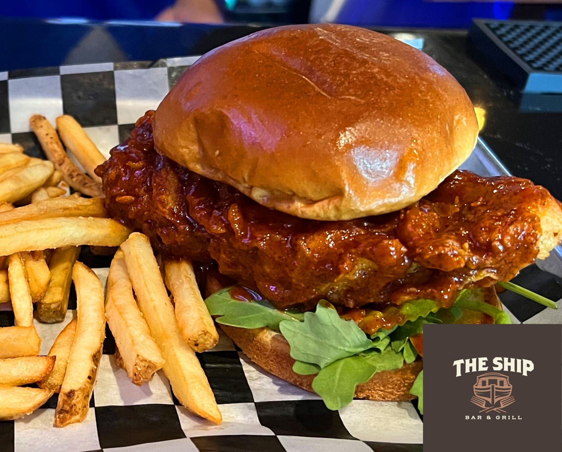 Chicken sandwich with fries on a checkered paper, served at The Ship Bar & Grill.