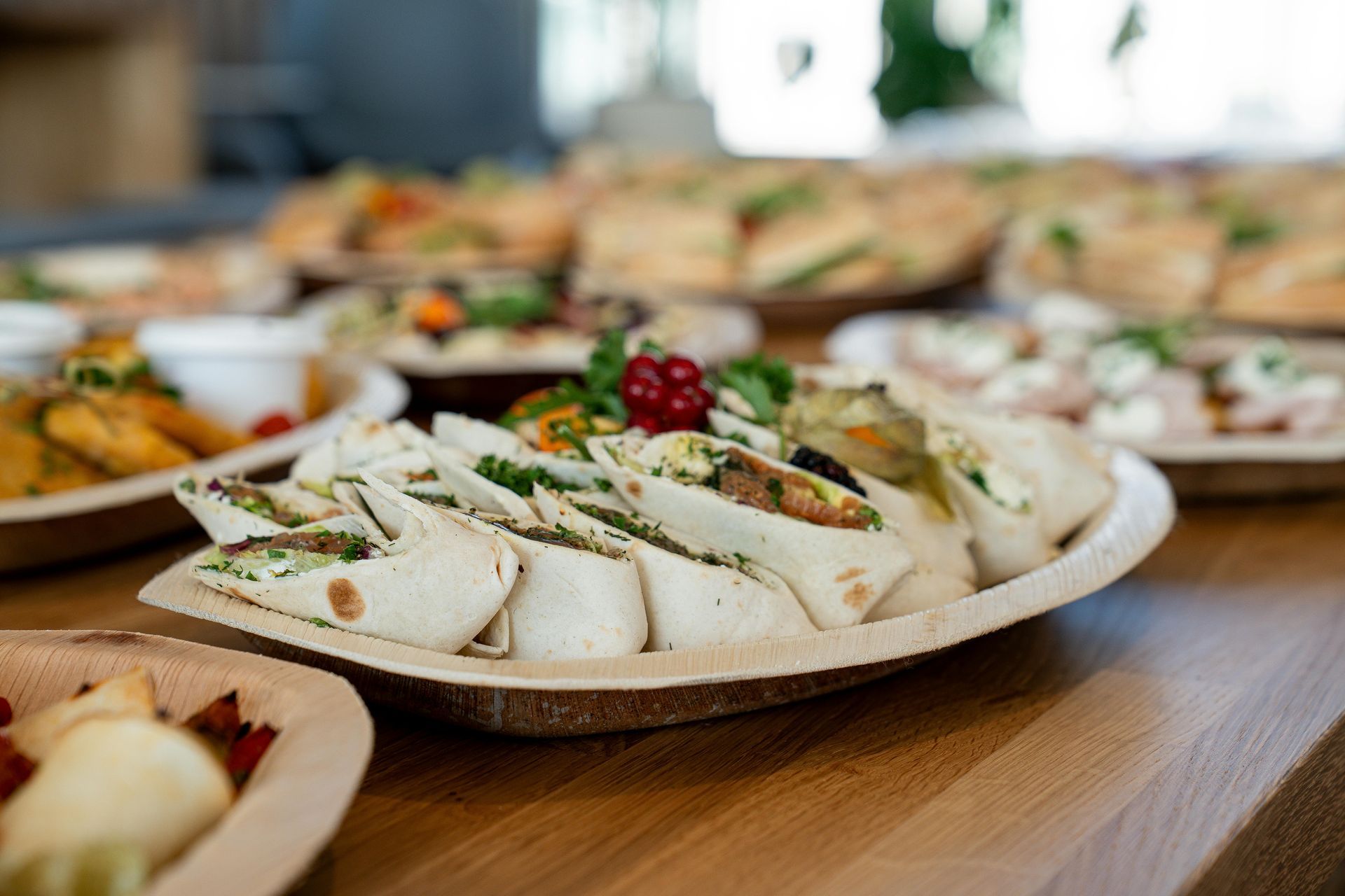Wraps, sandwiches, and salads arranged on a wooden table, possibly a catered event.