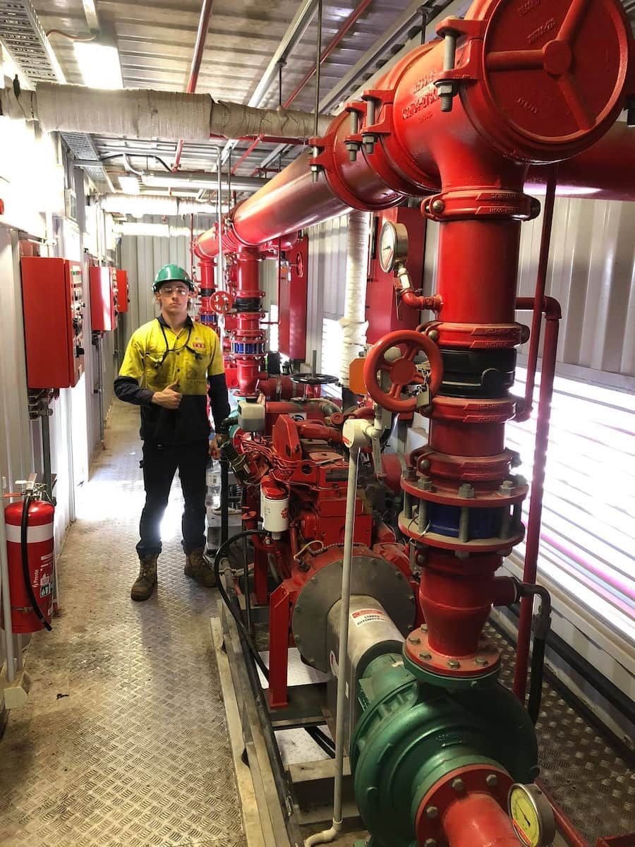 A Man Is Standing In A Hallway Next To A Bunch Of Red Pipes — TBR Mechanical in East Arm, NT