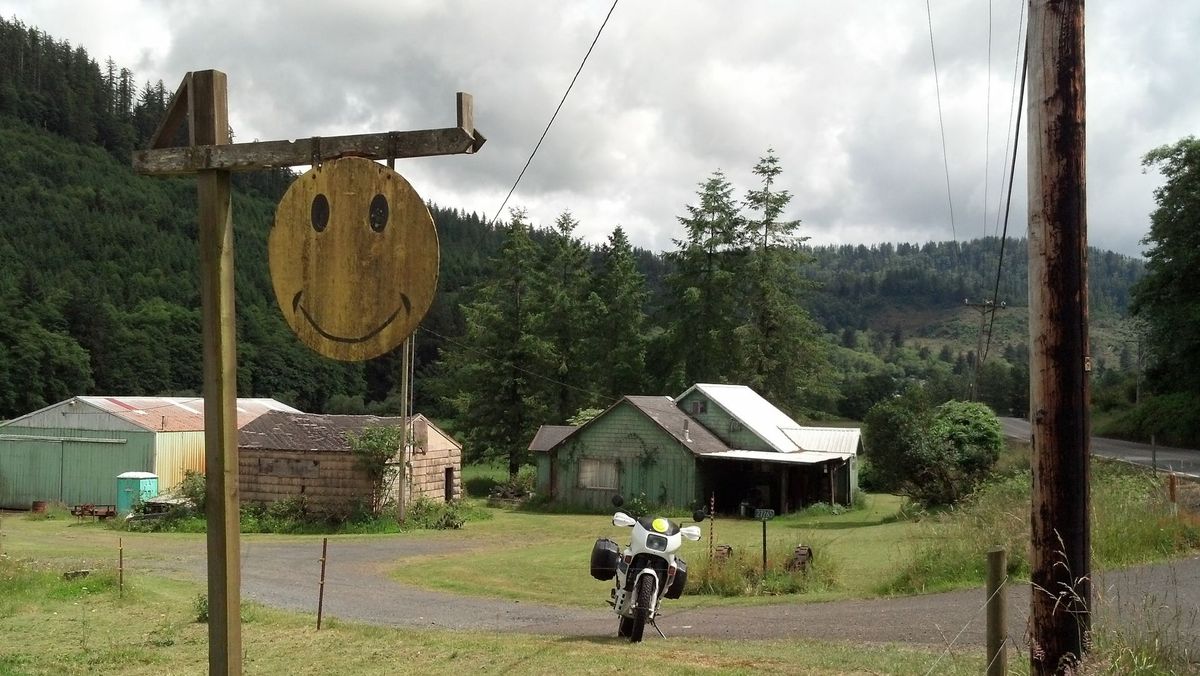 A weathered wooden smiley face sign on a farm with a motorcycle parked in the yard