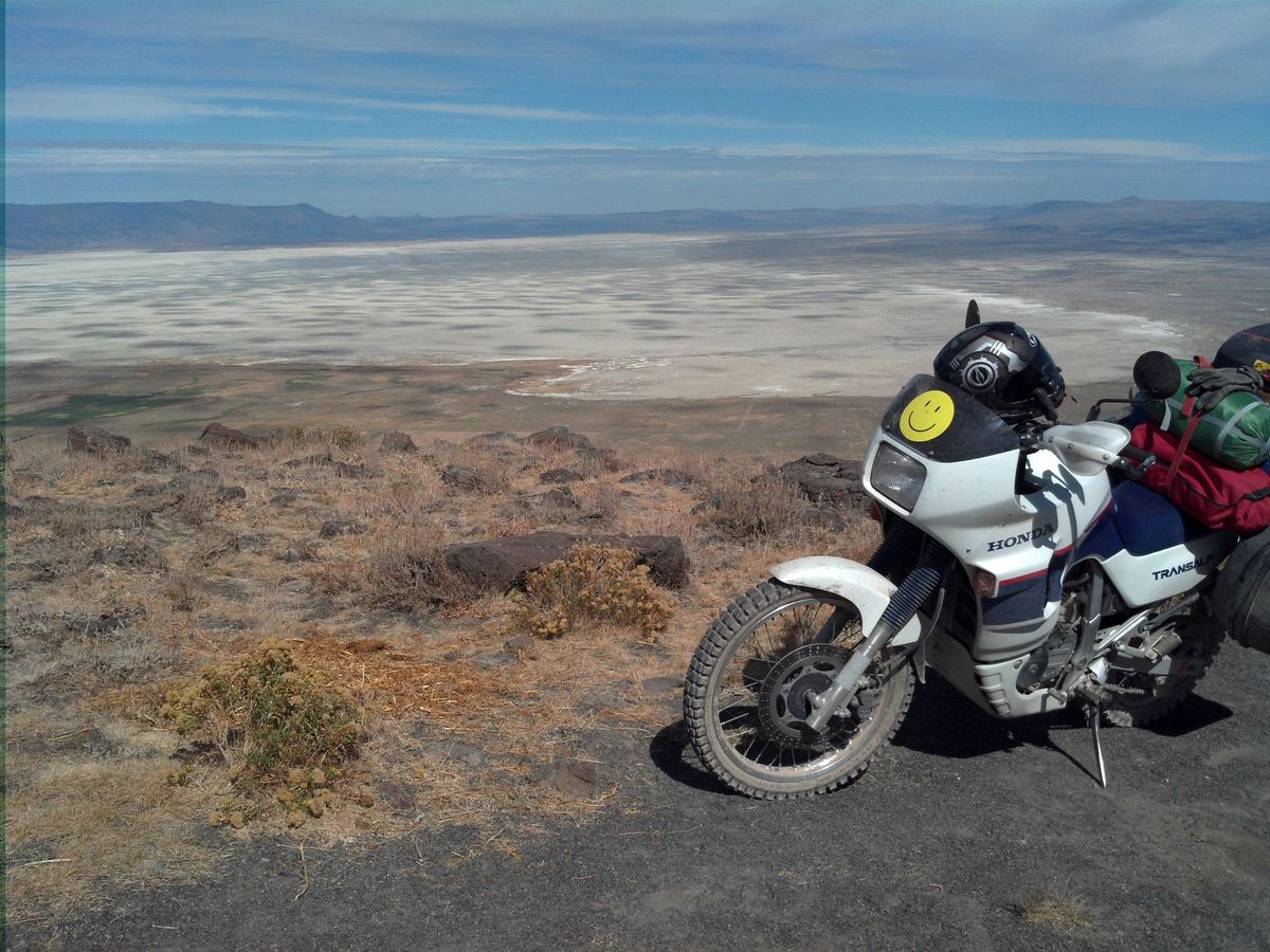 A Honda Transalp with a yellow smiley face on the fairing overlooking a vast dry lake bed