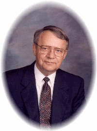Studio portrait of a man in a dark suit, white shirt, and patterned tie against a gray background