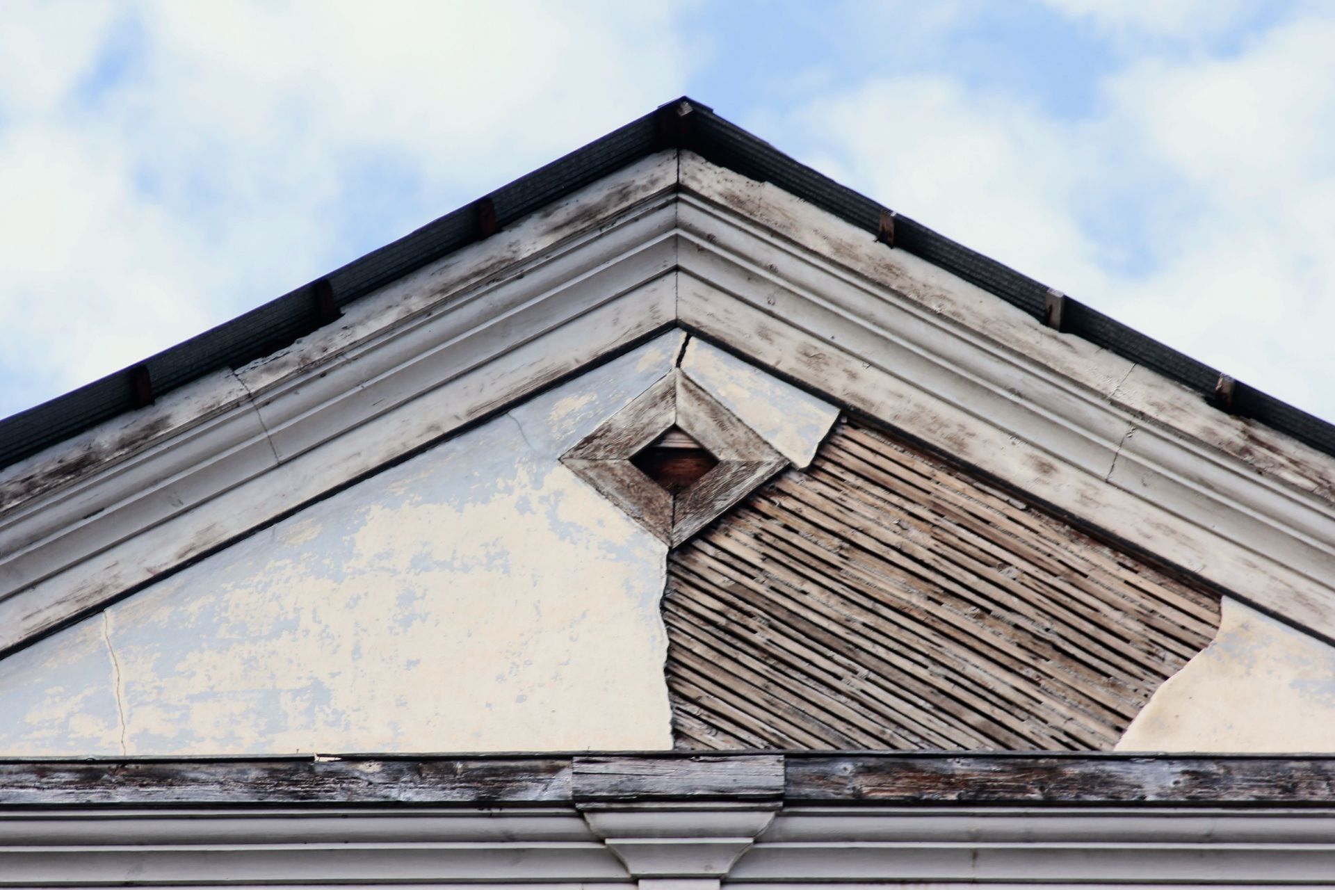 Damaged white gable wall with boarded opening,