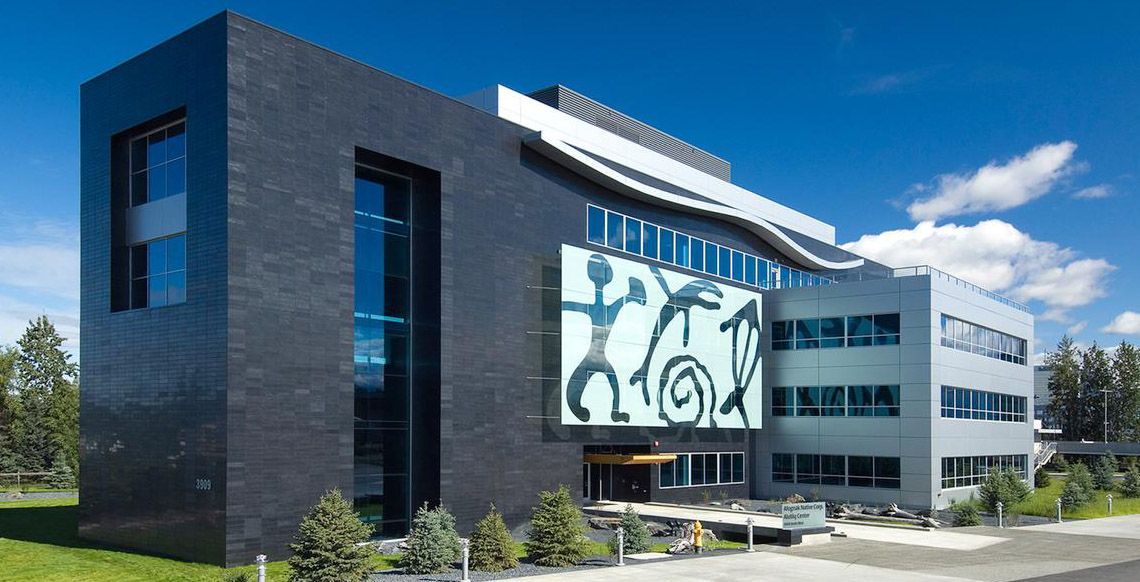 Modern, dark-gray building with abstract art on the facade under a clear, blue sky.