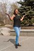 Woman with open arms, smiling, wearing jeans and black top, standing outside.