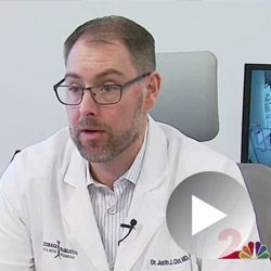 Doctor in a white coat speaking, wearing glasses, and a name tag.