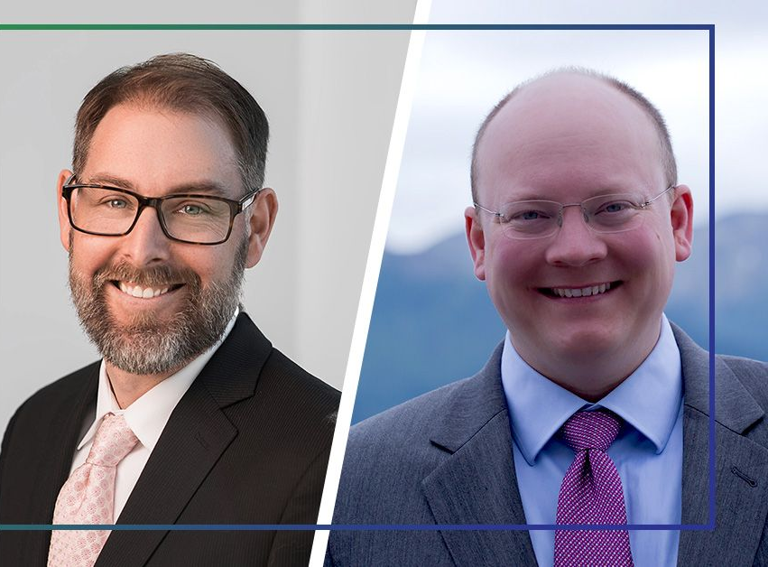 Two men in suits, smiling; one with glasses and a beard, the other with glasses and a tie.