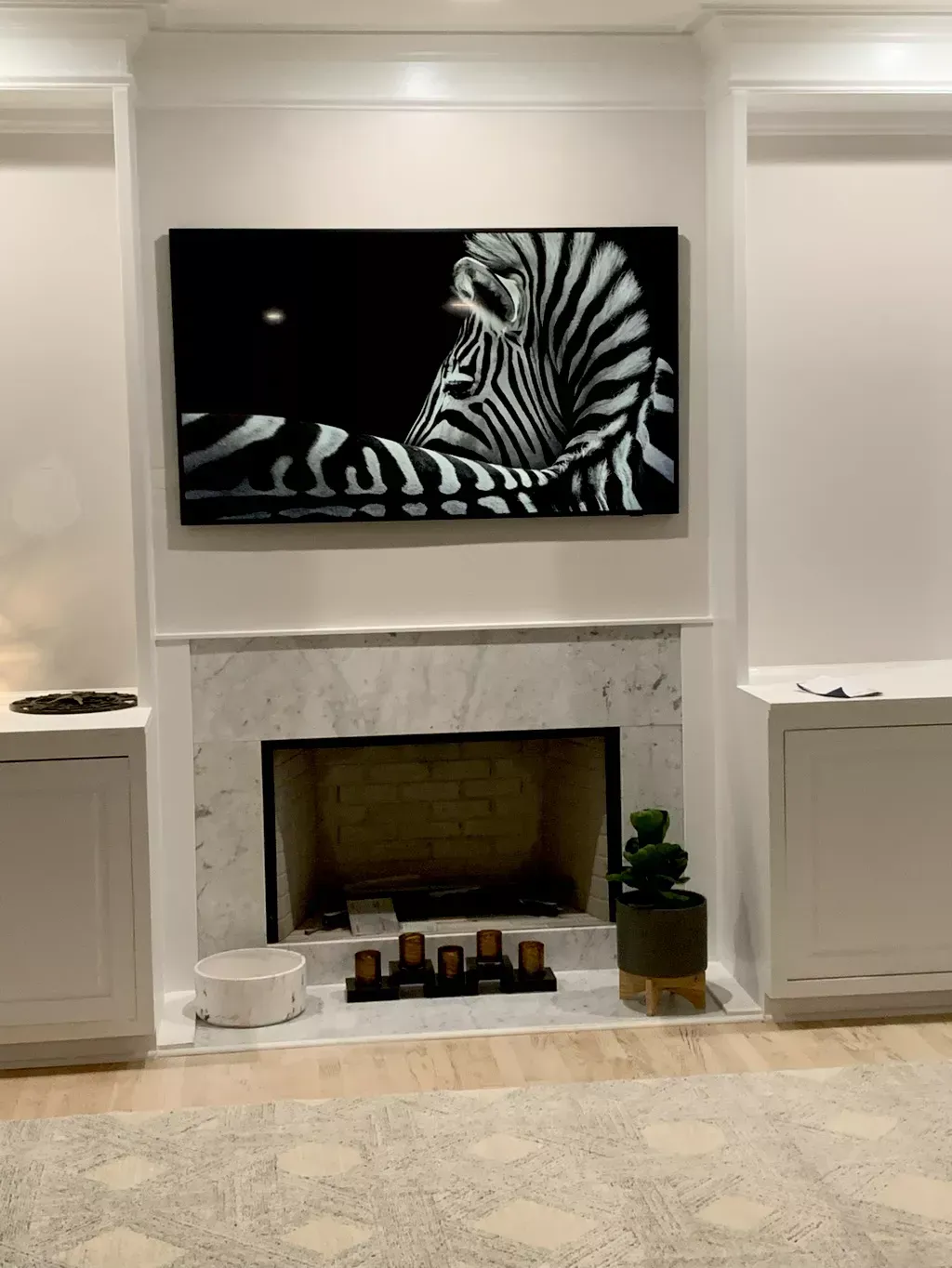 A living room with a fireplace and a zebra painting on the wall.