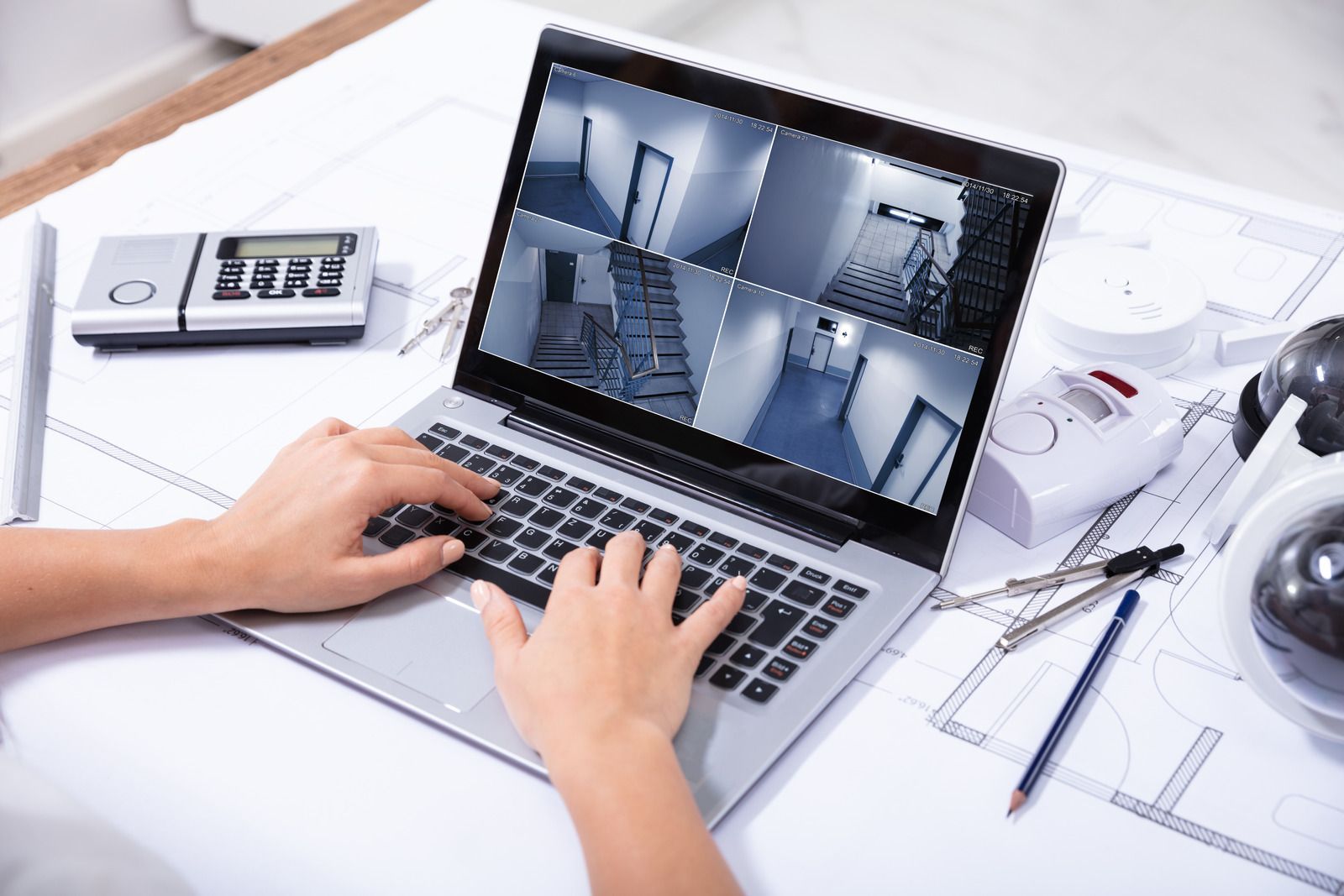 A person is typing on a laptop computer with a security camera on the screen.