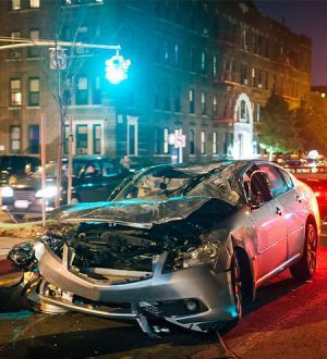 A damaged car is parked on the side of the road at night.