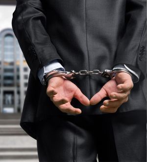 A man in a suit is wearing handcuffs behind his back