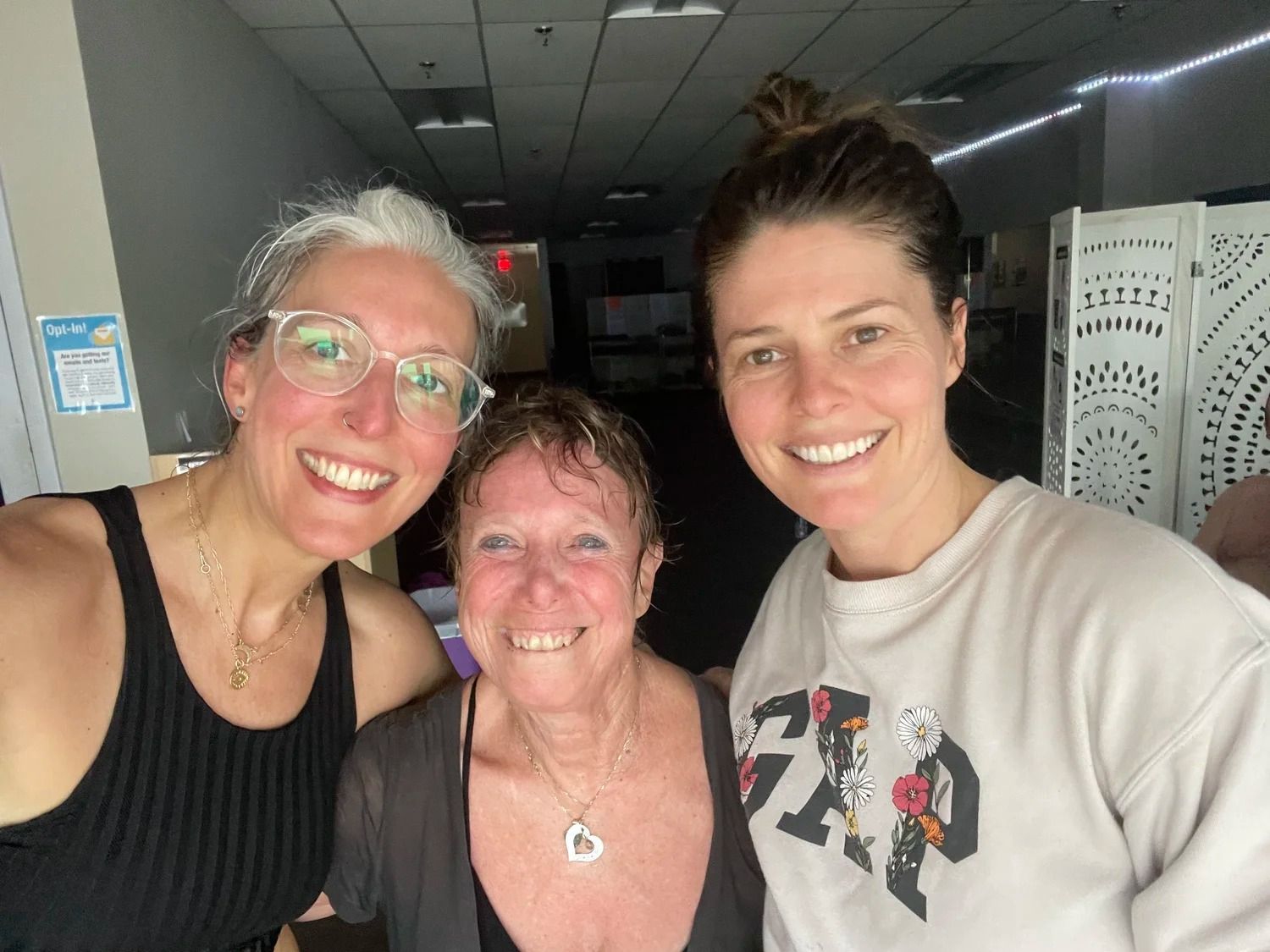 Three women smiling together for a close-up selfie in an indoor setting.