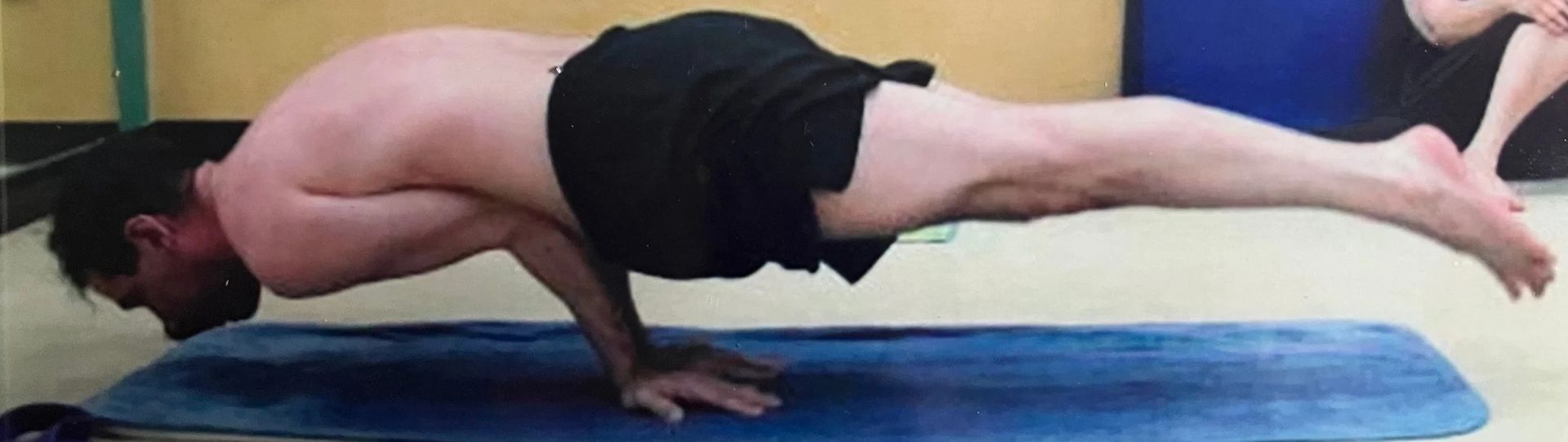 A person performs a peacock pose, balancing their body horizontally above a yoga mat with arms supporting their torso.