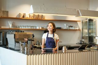 A woman is standing behind a counter in a Front's client restaurant holding a Front tablet.